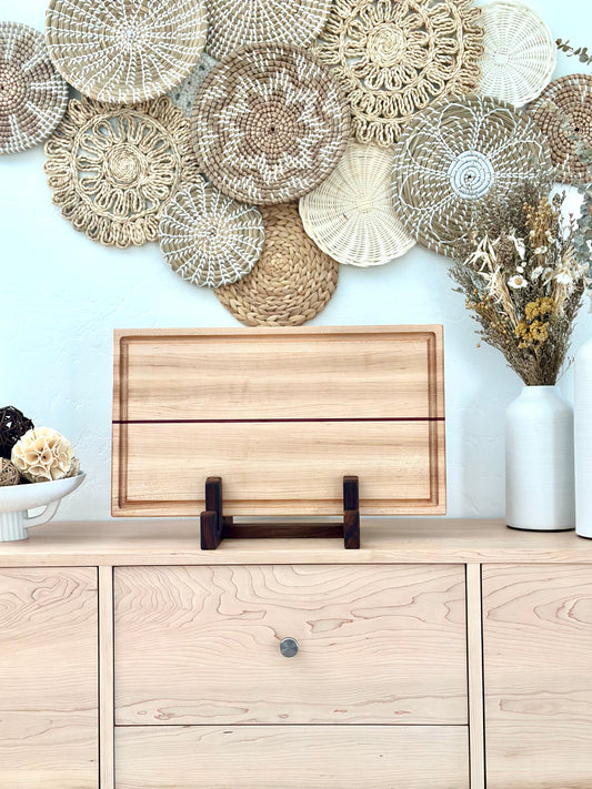 Bonobuilt maple cutting board No. 002, 22×13 in, with Purple Heart accent strip, displayed upright in a stand — handcrafted in Visalia, California
