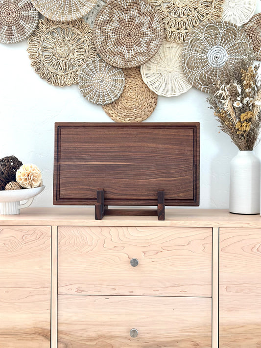 Bonobuilt walnut cutting board No. 001, 22×13 in, with juice groove, displayed upright in a stand — handcrafted in Visalia, California
