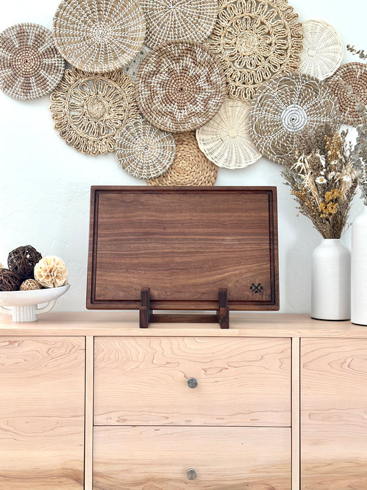 Bonobuilt walnut cutting board No. 004 Lite, 23×15 in, slim profile with juice groove, displayed upright in a stand — handcrafted in Visalia, California

